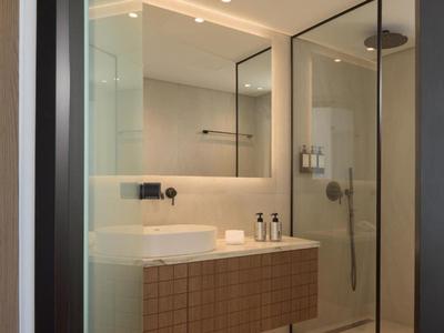 Baño moderno con ducha de cristal, espejo grande y lavabo sobre mueble de madera.