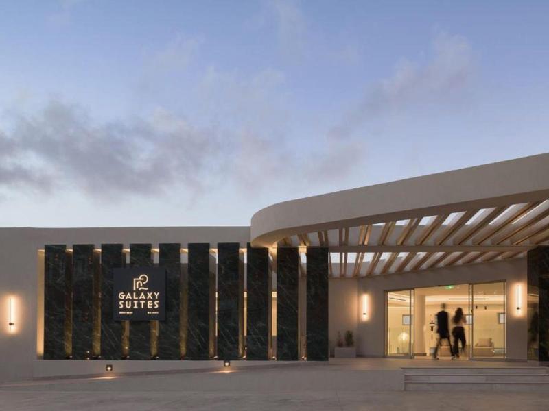 Edificio de hotel moderno con entrada iluminada al anochecer y dos personas en la puerta.