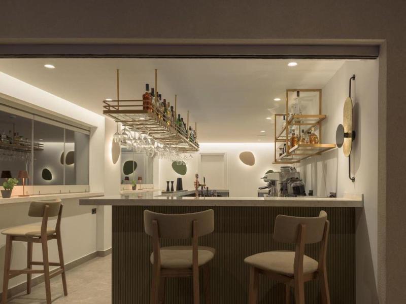 Bar moderno de hotel con taburetes de madera, estantes para vino y luz tenue.