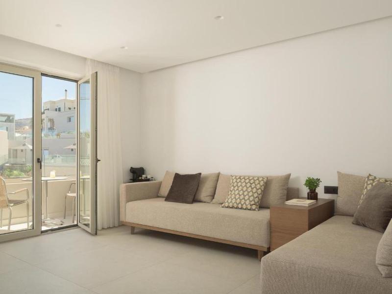 Sala luminosa con dos sofás, cojines y acceso a un balcón con vista a la ciudad.