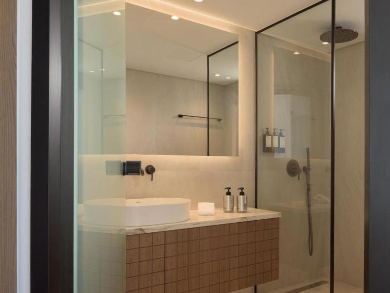 Baño moderno con ducha de cristal, espejo grande y lavabo sobre mueble de madera.