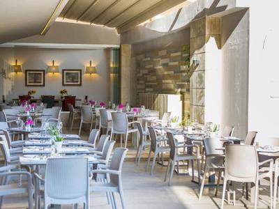 Restaurante luminoso con interior moderno, sillas y mesas blancas en un ambiente abierto.