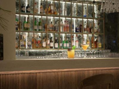 Bar moderno de hotel con estantes iluminados de licores y taburetes en la barra.