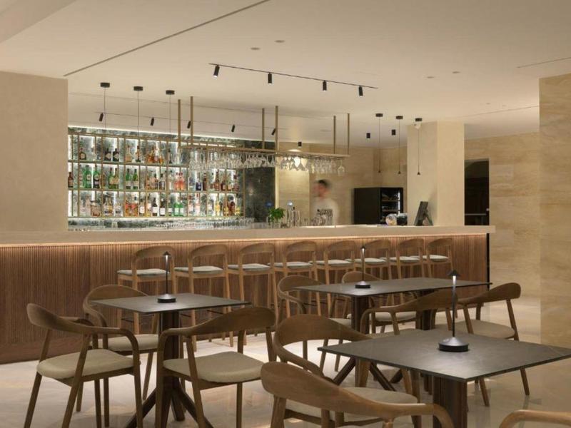 Elegant hotel bar with wooden chairs, tables and illuminated back wall shelving with bottles.