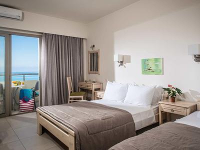 Camera d'hotel luminosa con due letti, scrivania, balcone e vista mare.