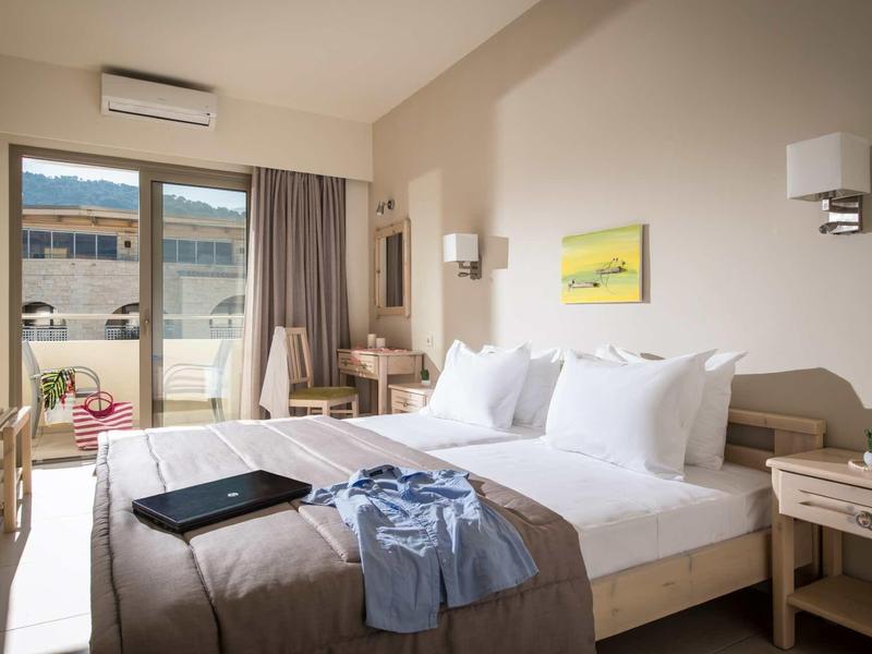 Helles Hotelzimmer mit Doppelbett, Balkon, schlichtem Holz-Mobiliar und neutralen Farben.