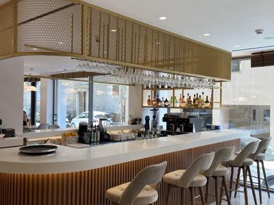 Moderní hotelový bar se zakřiveným dřevěným pultem a čalouněnými barovými židlemi