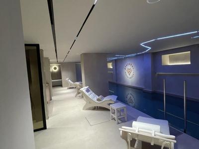 Area benessere moderna con lettini accanto a una piscina e soffitto illuminato indirettamente.