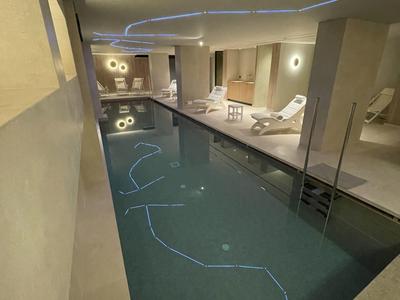 Piscina interna moderna con lettini e illuminazione indiretta in un hotel.