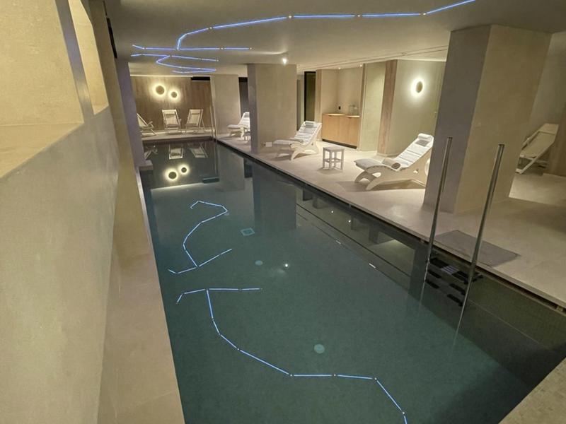 Piscina interna moderna con lettini e illuminazione indiretta in un hotel.