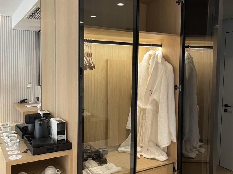 Armadio moderno in camera d'hotel con ante in vetro, accappatoio e accessori per il caffè.