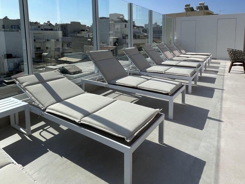 Fila di moderni lettini prendisole su una terrazza sul tetto con parapetto in vetro in una giornata di sole.