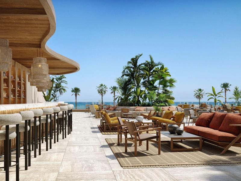 Moderner Außensitzbereich mit Holzmöbeln, hohen Barhockern, Pflanzen und blauem Himmel am Meer.