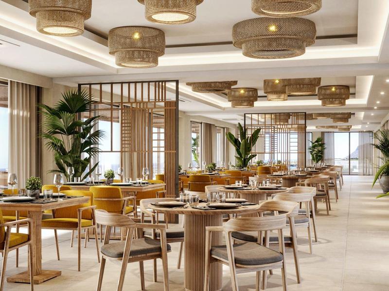 Heller, großzügiger Speisesaal mit Holzmöbeln, gelben Sesseln, Pflanzen und großen Fenstern.