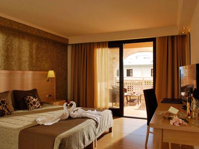 Gemütliches Hotelzimmer mit Doppelbett, Balkon und Holzmöbeln bei warmem Licht.