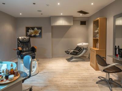 Modern eingerichteter Friseursalon mit Stühlen, Spiegeln und einem Massagestuhl in warmem Licht.