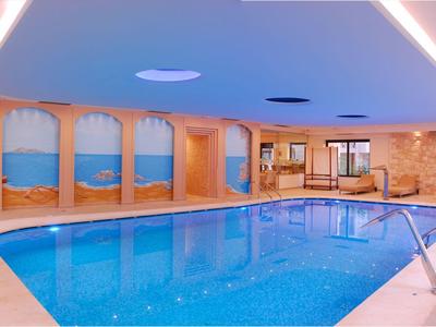 Innenhotel-Pool mit blauem Wasser, beigen Fliesen und Wandbildern von Wüstenlandschaften.
