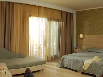 Gemütliches Hotelzimmer mit Doppelbett, Sofa und Vorhängen vor Balkonfenstern.