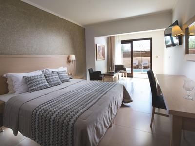 Helles Hotelzimmer mit großem Bett, Schreibtisch, Stühlen und Terrasse mit Aussicht.