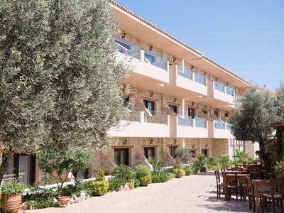 Ein Hotelgebäude mit Balkonzimmern und schattiger Außensitzgelegenheit, umgeben von Bäumen.