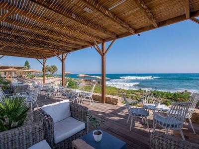 Überdachte Terrasse mit Sitzgelegenheiten am Meer und Blick auf den Ozean bei klarem Himmel.