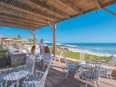 Überdachte Terrasse mit weißen Stühlen und Blick aufs Meer bei klarem Himmel.