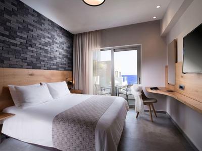 Modernes Hotelzimmer mit großem Bett, dunkler Steinwand, Schreibtisch und Balkon mit Meerblick.