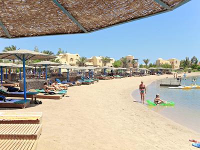 Zonnig strand met ligbedden, parasols, mensen die zwemmen en ontspannen bij het water.
