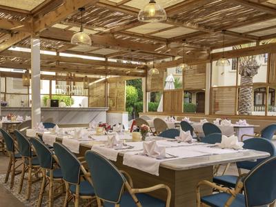 Grande salle à manger extérieure avec tables dressées et chaises bleues sous un auvent en bois.