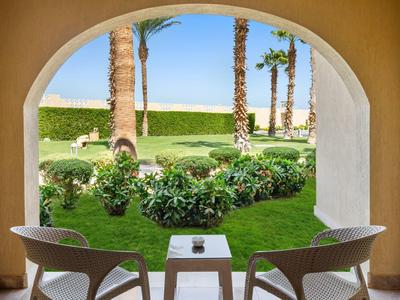 View through an archway onto a garden with palm trees and green plants, two chairs and a table in front.