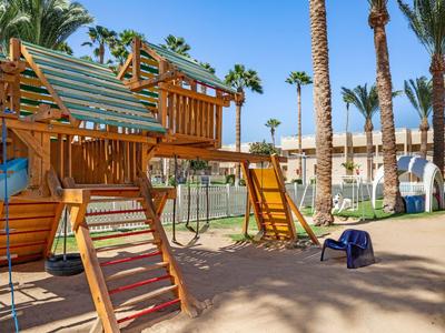 Children's playground with climbing frames and slides in a sunny hotel area with palm trees.