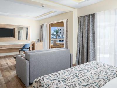 Modern hotel room with bed, sofa, desk, and large window with curtains.