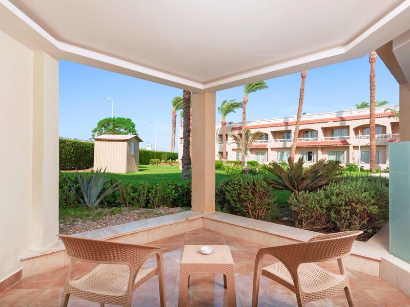 Outdoor seating area with two chairs and a table on a patio, overlooking a garden and hotel building.