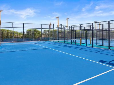 Leerer blauer Paddle-Tennisplatz unter klarem Himmel mit Umzäunung und Bänken.