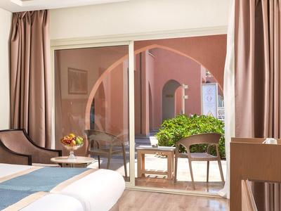 Habitación de hotel con vista a una terraza con plantas verdes y paredes rosas a través de una gran puerta corrediza de vidrio.