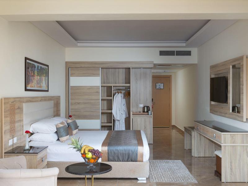 Habitación de hotel con cama doble, armario, mesa y silla en tonos neutros y diseño moderno.