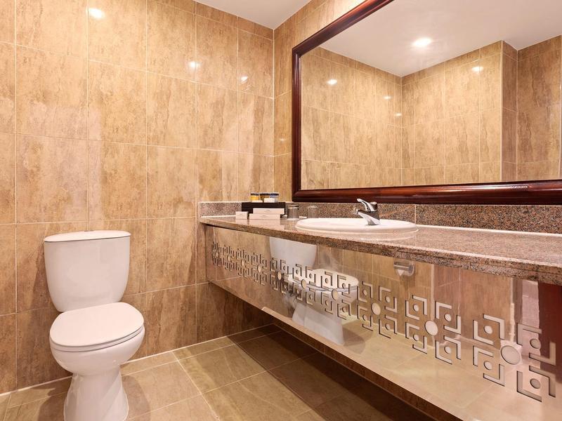 Baño moderno con inodoro blanco y tocador amplio con espejo grande y paredes beige.