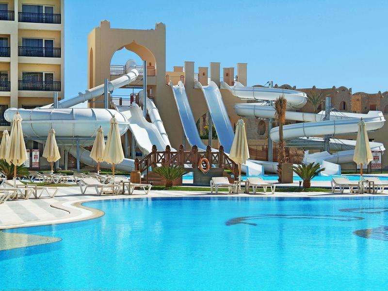 Grand piscine d'hôtel avec toboggans aquatiques et chaises longues sous parasols.