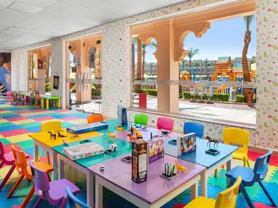 Kleurrijke speelruimte voor kinderen met tafels, kleine stoelen en knutselmaterialen bij grote ramen.