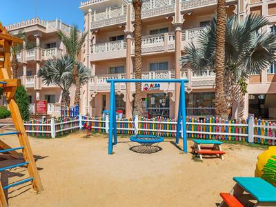 Spielplatz mit Schaukel und Klettergerüst vor einem Hotelgebäude und Palmen