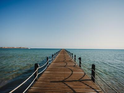 Ein langer hölzerner Pier, der sich ins ruhige blaue Meer unter klarem Himmel erstreckt.