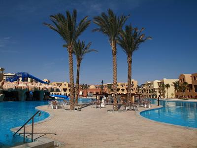 Großer Pool mit Palmen und Sonnenliegen in einer schönen Hotelanlage unter blauem Himmel.