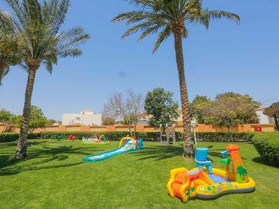 Kinderspielplatz mit Rutschen und grüner Wiese unter Palmen in Hotelanlage.