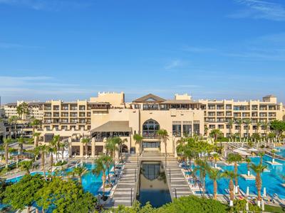 Luxe resort met grote zwembaden, palmbomen en een heldere blauwe lucht.