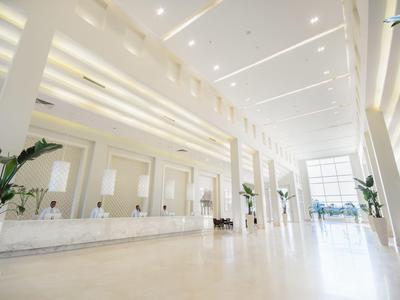 Helle und moderne Hotellobby mit einer langen Rezeption, großen Fenstern und Pflanzen.