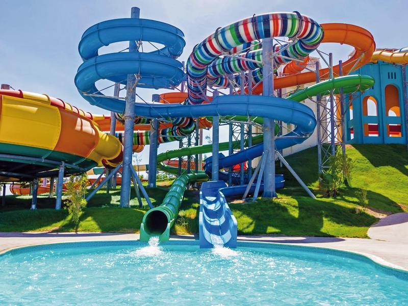 Toboganes de agua en un parque acuático con piscina y césped verde alrededor.