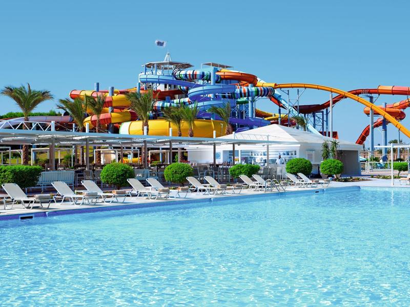 Gran parque acuático con toboganes de colores junto a una piscina con tumbonas.