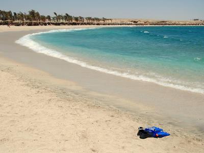 Empty sandy beach with blue sea and clothes on the shore under clear sky.