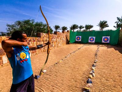 Persona apunta con arco a tres dianas en un campo de tiro con cerca de madera natural.