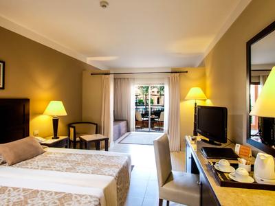 Bright hotel room with two twin beds, desk, TV, and balcony access.